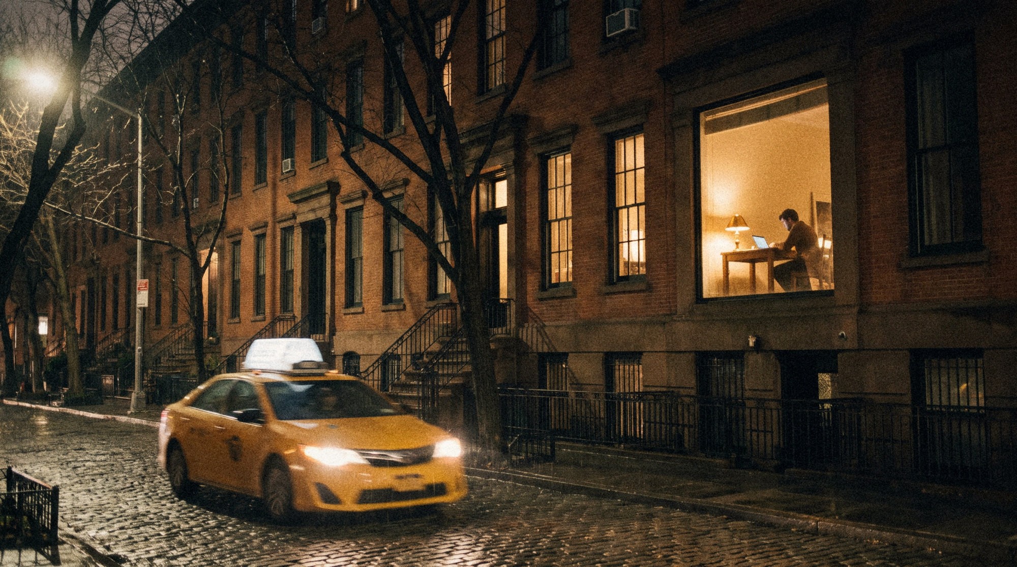 A single illuminated window on a West Village brownstone street, with someone working at a desk